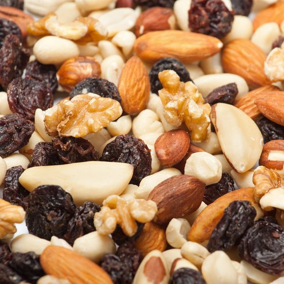 Verschiedene Nüsse (Walnüsse, Haselnüsse, Cashews Pecannüsse und Erdnüsse) sowie Rosinen liegen auf einem Tisch.